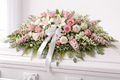 Floral arrangement on a white casket with pink and white flowers and a white ribbon.