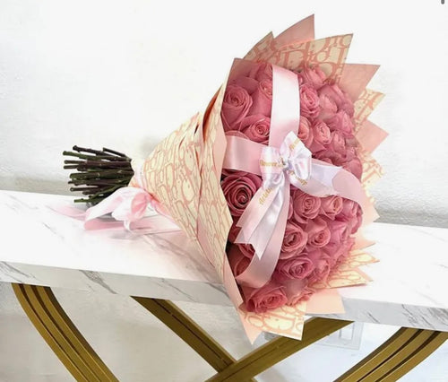 Bouquet of pink roses wrapped in cellophane with a white ribbon on a white surface.
