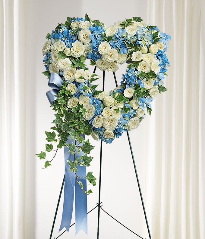 Heart-shaped floral arrangement with white and blue flowers on a stand against a white background