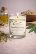 Candle labeled 'Emite Creations Soothing Hemp' with cannabis seeds and leaves on a wooden surface.